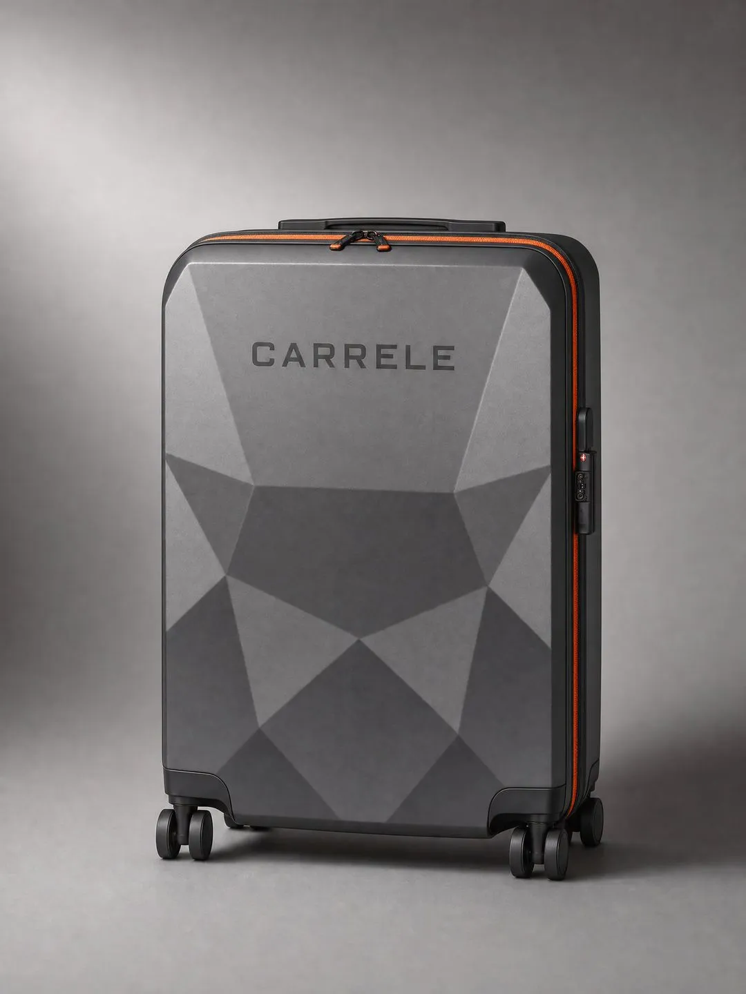 Faceted graphite Carrele suitcase with an orange zip on a grey studio backdrop.