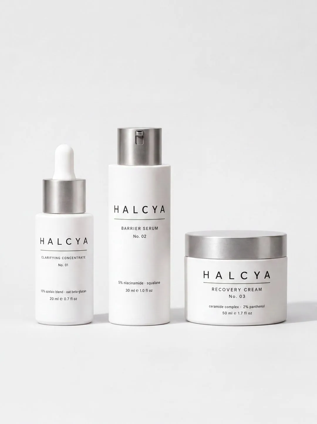 Three Halcya skincare products on white: a dropper bottle, a pump bottle and a jar, each with a brushed steel cap.
